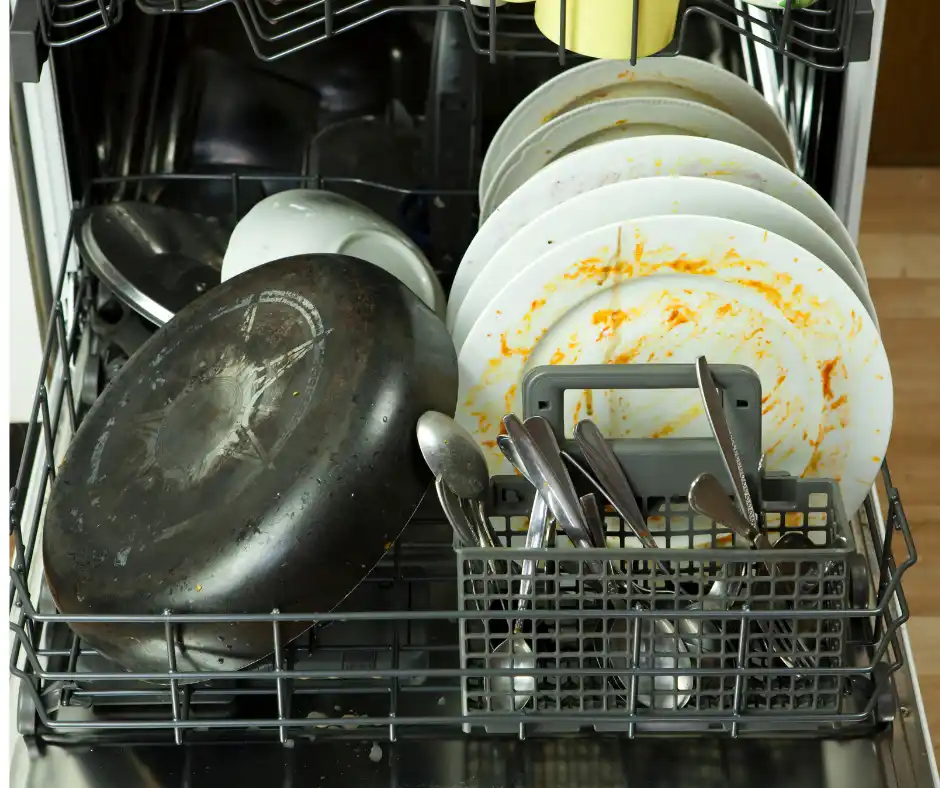 Dirty plates, cutlery, and frying pan inside a dishwasher before kitchen cleaning